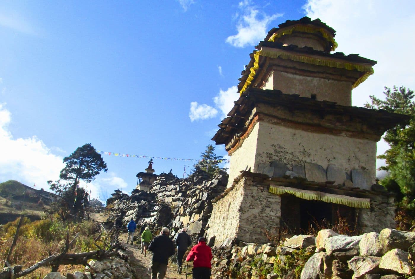 Hikers walking towards ancient stone stupa in Tsum Valley, Nepal, under a bright blue sky