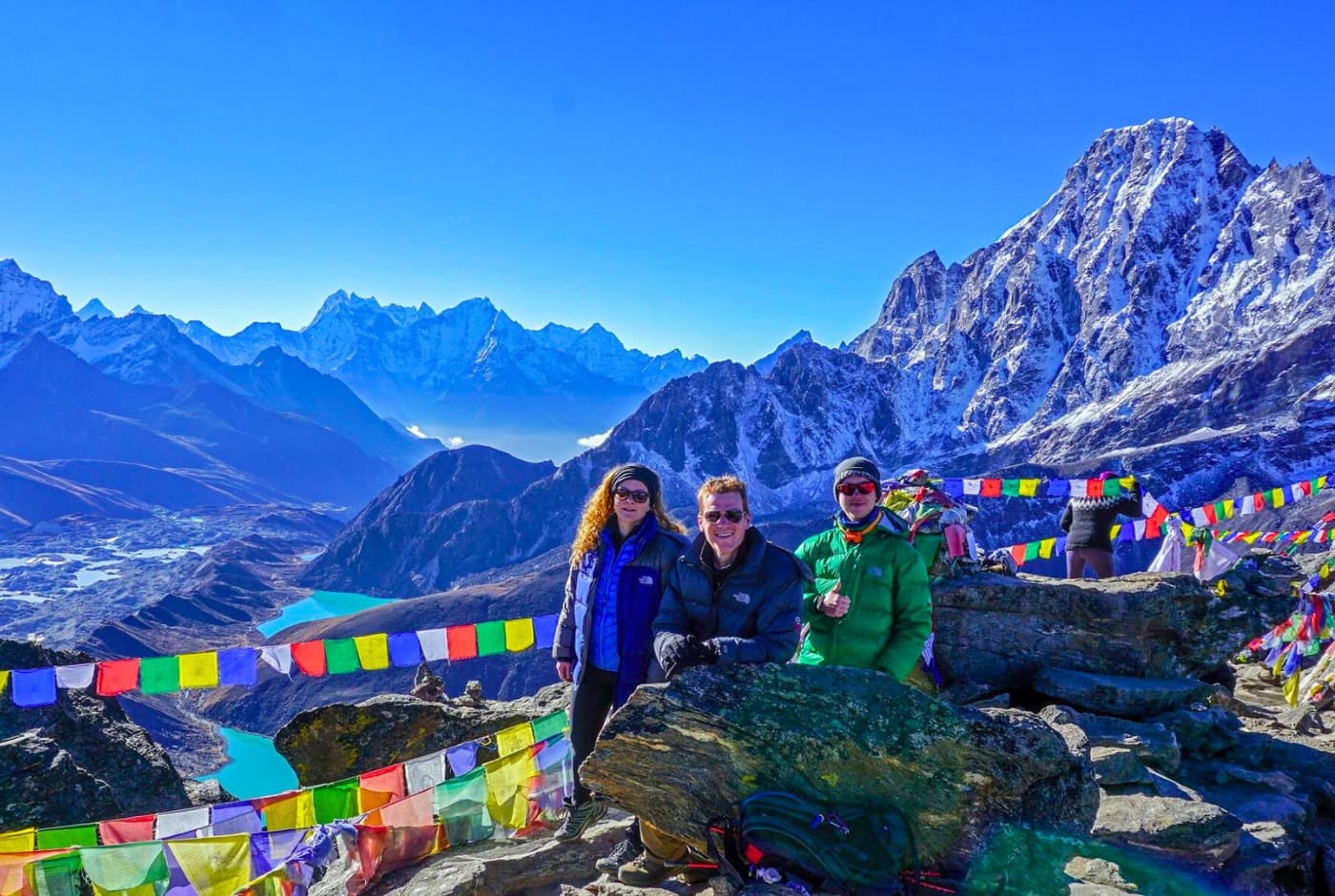 Three trekkers posing with a thumbs-up on a mountain trek with Everest and other peaks