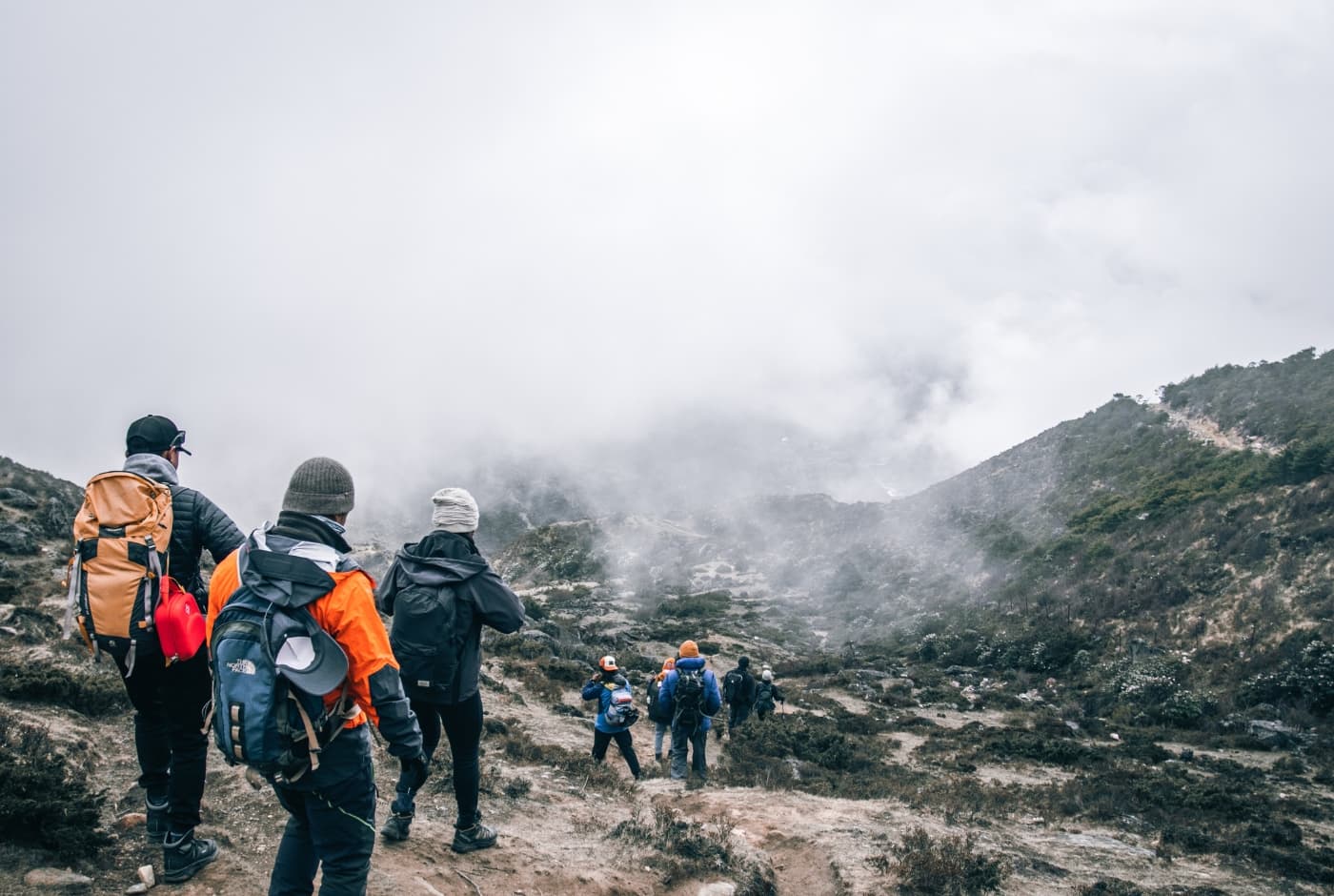 A group of trekkers wearing backpacks and warm clothing hike through a foggy to Thame cillage   Everest