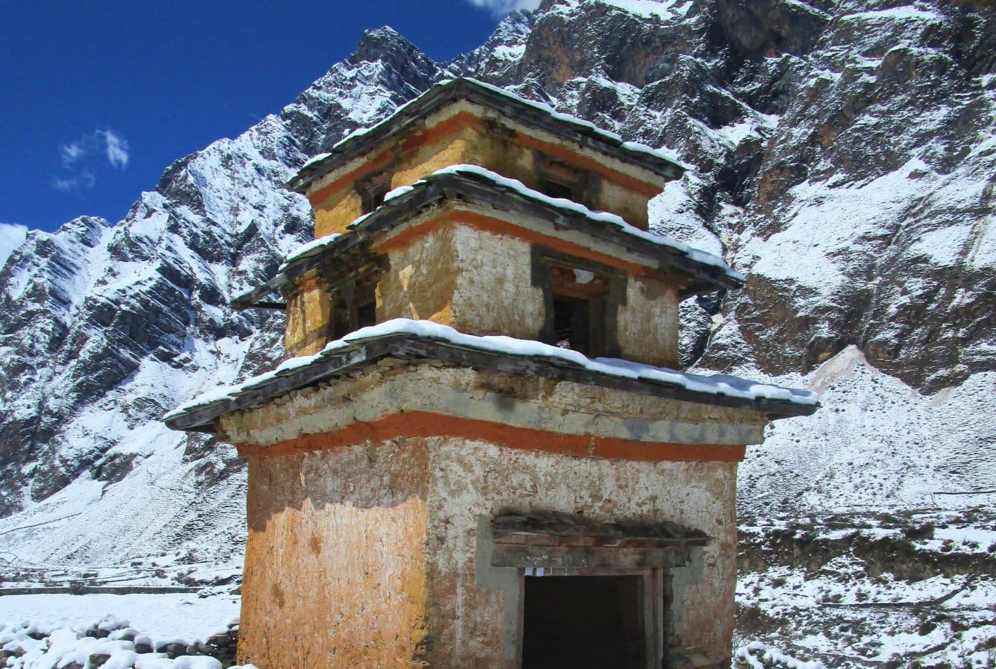 Old stone stupa with snow Covered roof, set against the backdrop of rugged, snowy mountains in Tsum Valley