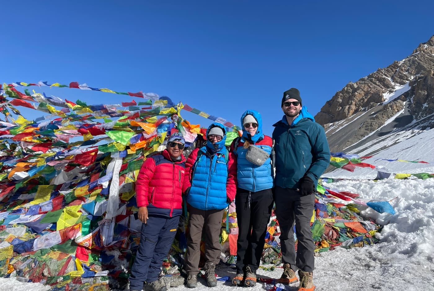 Trekkers at Thorong La Pass on the Annapurna Circuit, with colorful prayer flags and snow Capped mountains