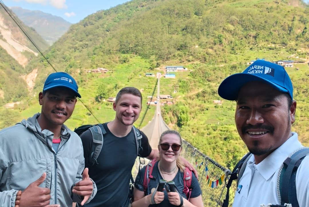 Nepal Hiking Team guides and trekkers on suspension bridge over Modi Khola with terraced hillsides on final day hiking from Jhinu Danda to Samrung