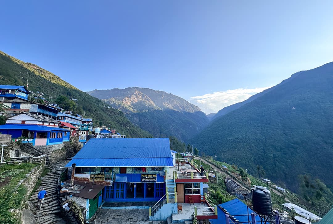 Ulleri village teahouses with blue roofs on terraced hillside at 1960 meters during Annapurna Base Camp trek with Himalayan mountain peaks in background