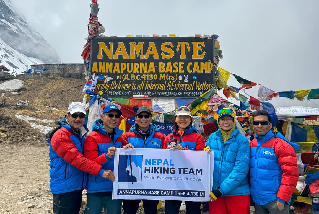 Nepal Hiking Team Guides And Trekkers Posing With Company Banner At Annapurna Base Camp 4130 Meters Signboard With Prayer Flags Before Descending To Bamboo