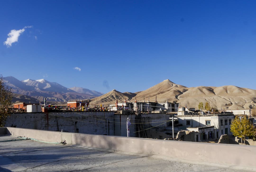 Rooftop View Of Lo Manthang Walled City With Barren Sandy Hills And Snow Capped Peaks