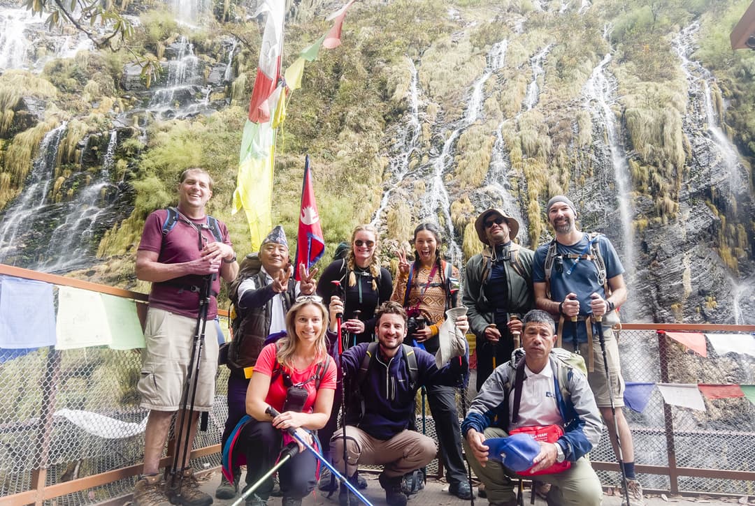 Trekker at Pujinim Barah temple shrine with prayer flags and waterfall
