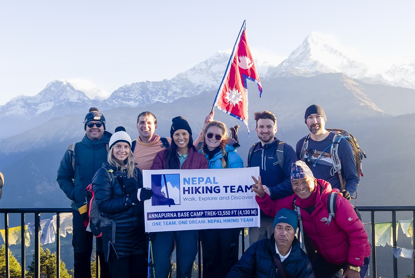 Group of trekkers holding Nepal Hiking Team banner at Ghorepani Poon Hill with Annapurna South behind